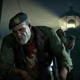Bill from Left 4 Dead looks at the ground while other L4D characters stand behind him at night.